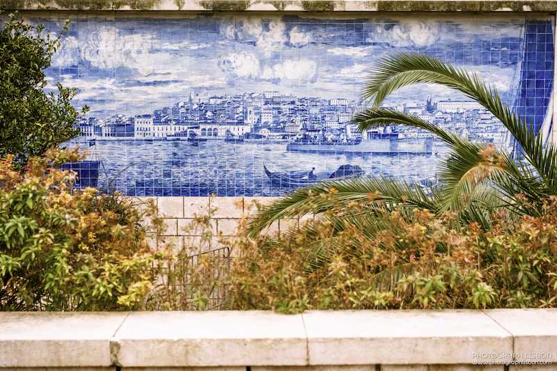 Hand-painted blue azulejo panel depicting Lisbon and the Tagus, framed by palm fronds at Miradouro de Santa Luzia, Alfama.