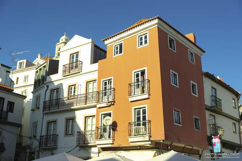 Terracotta and cream facades with wrought-iron balconies against a clear blue sky in Alfama, Lisbon.
