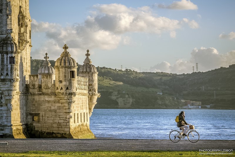 Belém Tower at golden hour with a cyclist passing along the Tagus riverside, Lisbon.