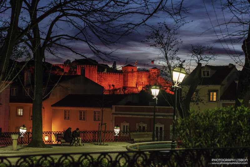 São Jorge Castle lit in red against the blue hour sky, seen from the streets below, Lisbon.